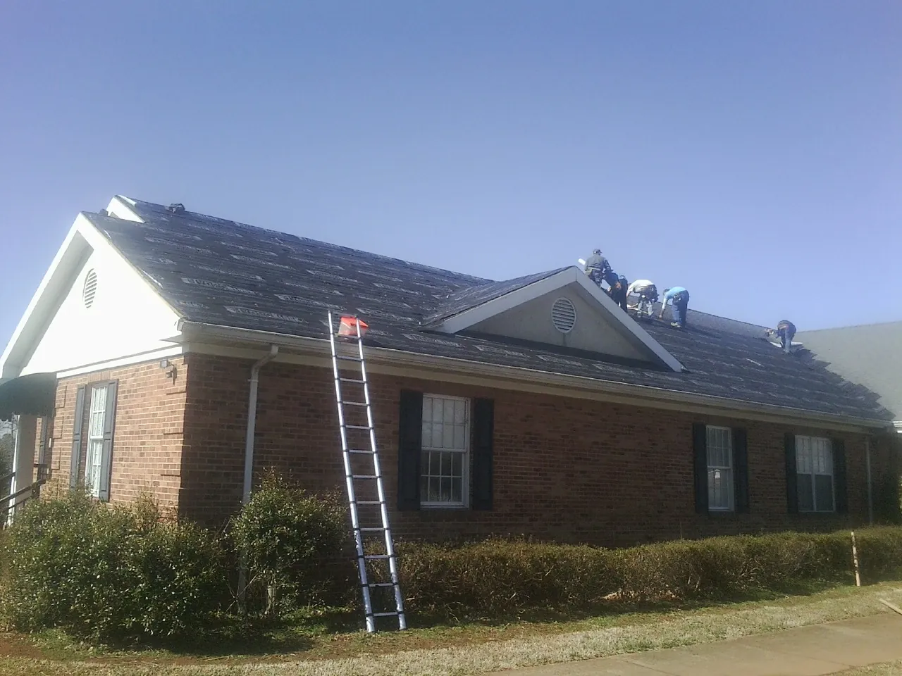 Crew tearing shingles off a brick ranch roof with a ladder set — Metal Roof Repair work by our crew in Damascus
